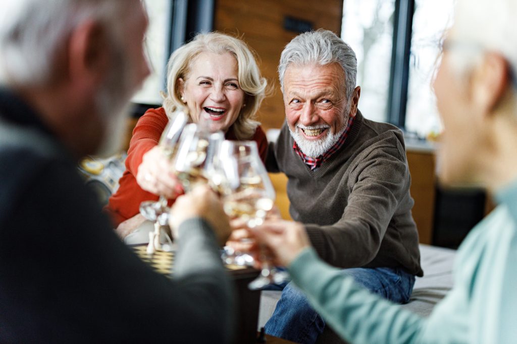 Happy senior couples toasting with white wine at home.